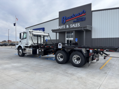 Volvo VHD64B300 truck in service bay area showing flatbed roll-off body and dual rear axles with hydraulic ramps.