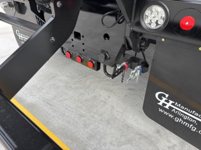 Front hitch area of a new Volvo VHD64B300 rolloff truck showing hydraulic lines and wiring, circular marker lights, and GV logo plate.