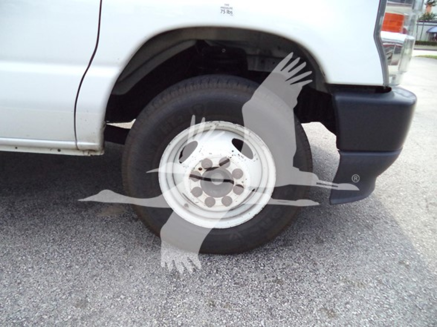 Ford E-350 wheel area showing front right tire and wheel well, partial bumper; stock photo with watermark overlay.