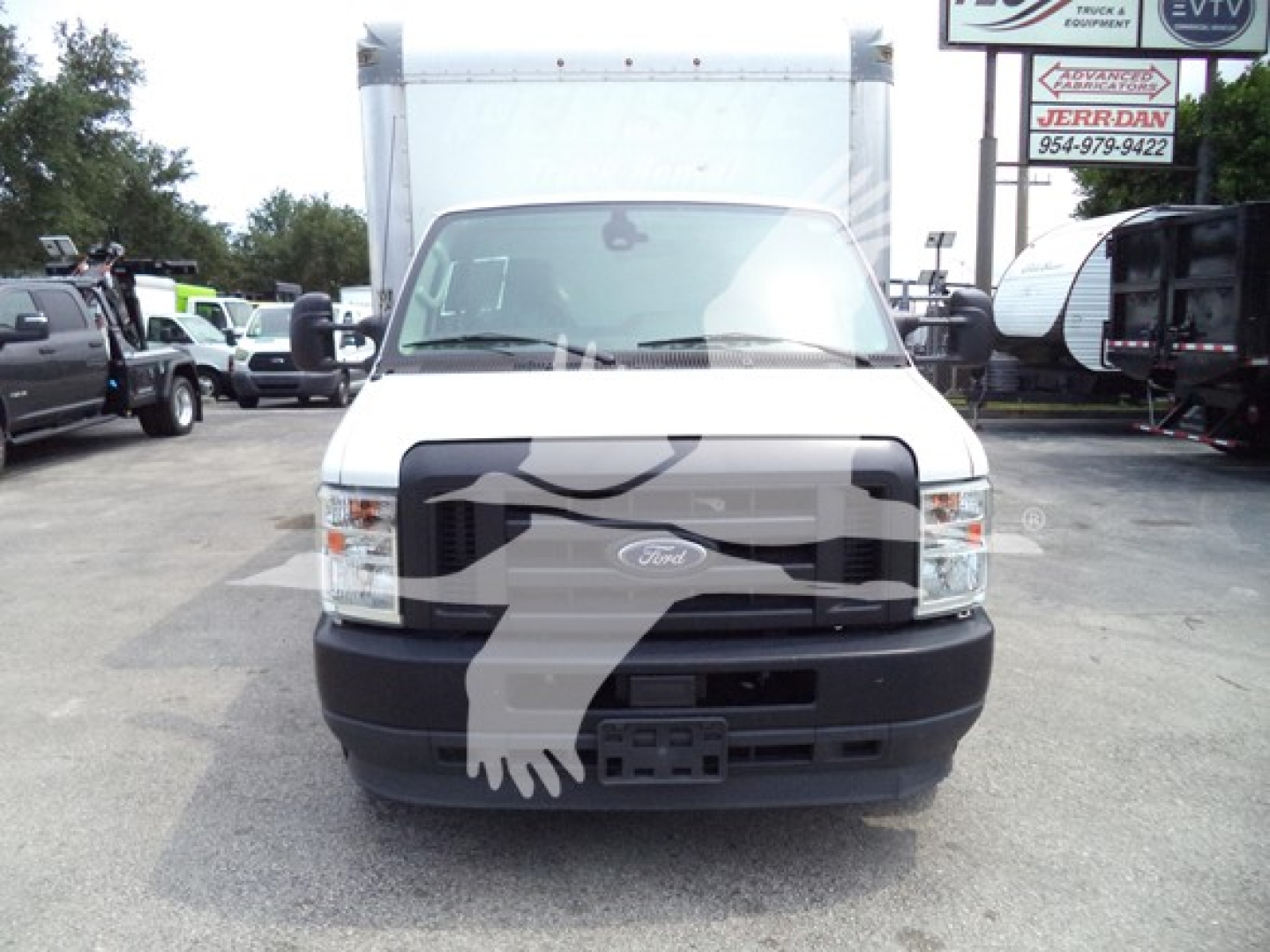 Ford E-350 front view showing grille, headlights, and bumper with large cargo box in background; dealership lot with other trucks nearby.