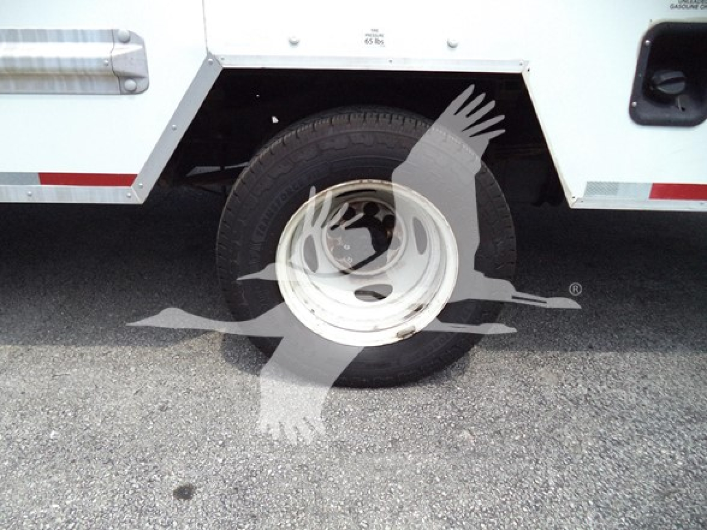 Truck wheel and side panel of a 2022 Ford E350 cutaway showing wheel, tire, and partial body with branding sticker.