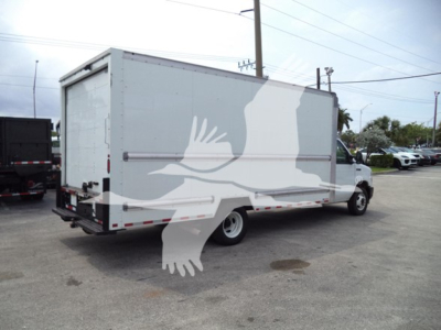 Box truck with a large cargo box showing a white silhouette graphic overlay on the side and rear; rear doors visible, urban lot in background.