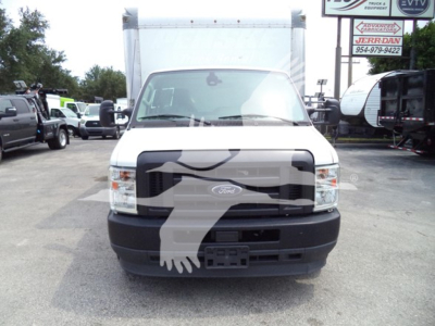 Ford E-350 front view showing grille, headlights, and bumper with large cargo box in background; dealership lot with other trucks nearby.