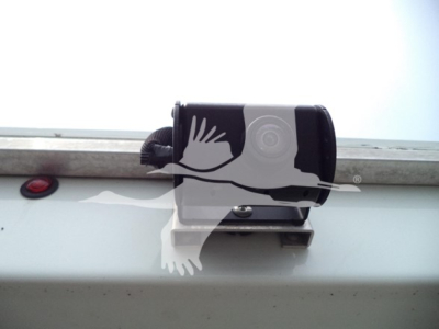 Rear view camera or sensor atop a high cube truck showing mounting bracket and small circular sensor.