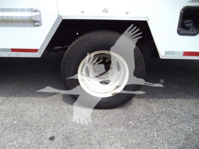 Truck wheel and side panel of a 2022 Ford E350 cutaway showing wheel, tire, and partial body with branding sticker.