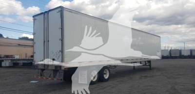 Trailer side view showing a long gray dry van trailer with dual rear wheels and rear doors.
