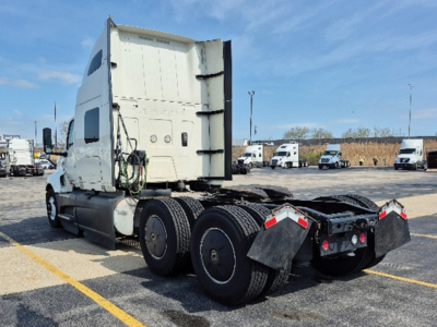 Truck tractor in a lot showing rear view with fifth wheel and dual rear axles, white cab, and various hoses; no visible text legible on components.