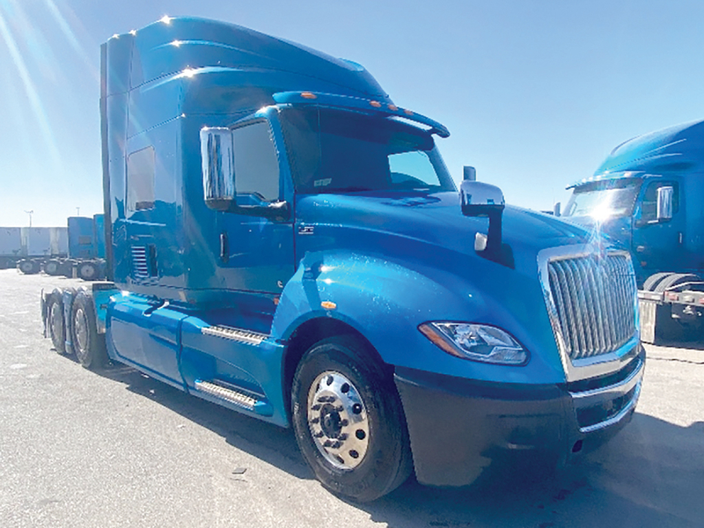 Truck cab showing large blue International LT625 sleeper with chrome grille and dual tires, side steps, and fuel tanks.