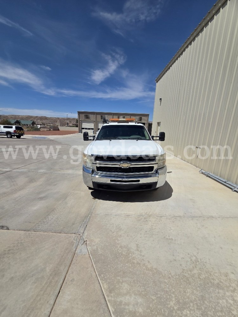 Chevrolet Silverado 3500HD front view in a driveway with clear sky, large chrome bumper, Chevy grille, and side mirrors visible.