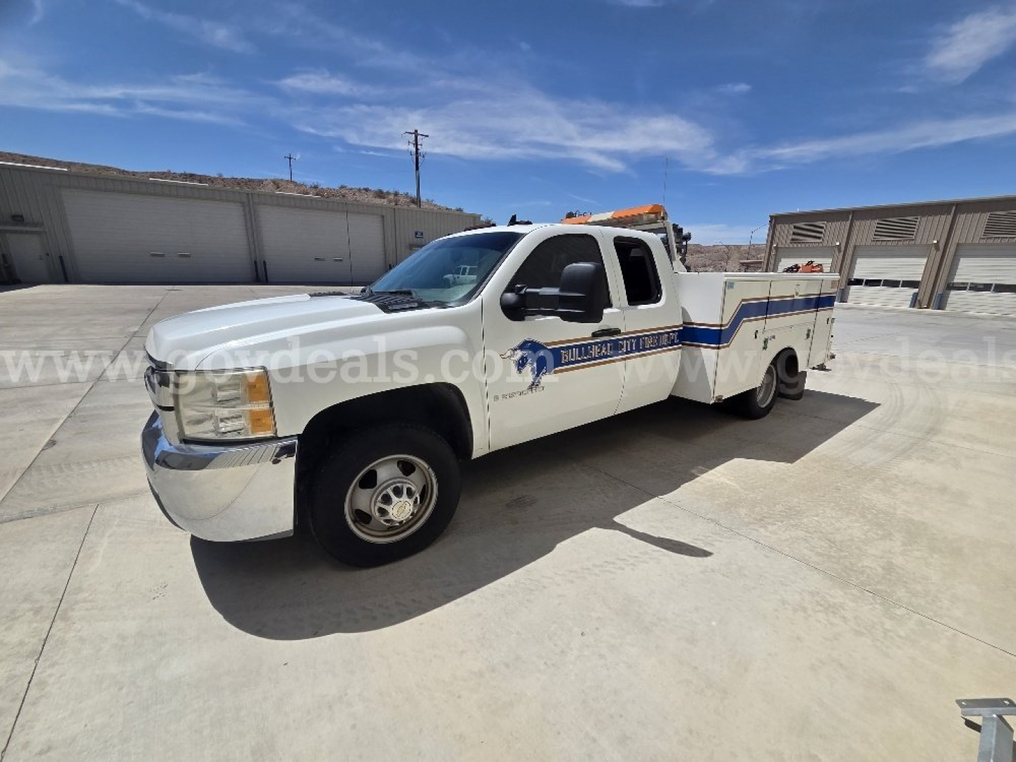 Chevrolet Silverado 3500HD service/utility truck in white with blue stripe and equipment bed, side view showing crew cab and rear aluminum utility bed.