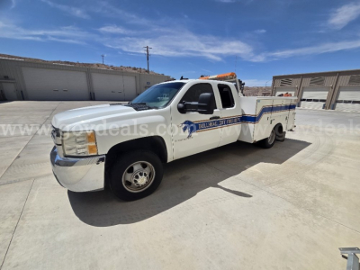 Chevrolet Silverado 3500HD service/utility truck in white with blue stripe and equipment bed, side view showing crew cab and rear aluminum utility bed.