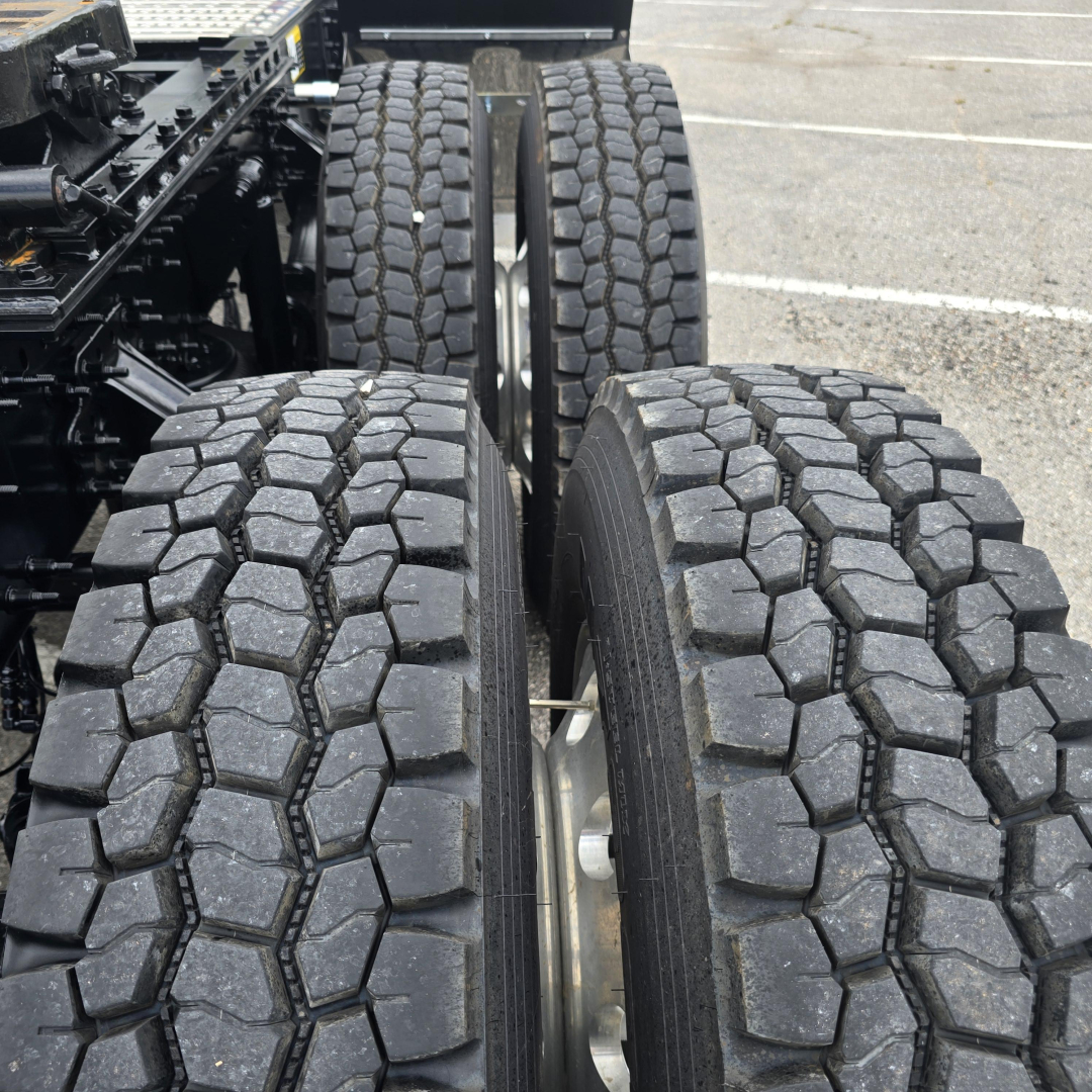 Truck chassis with dual rear axles and chunky off-road tires showing tread pattern and wheel hubs.