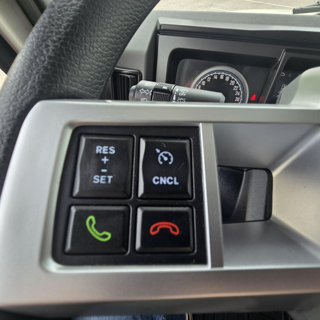 Steering wheel controls and dashboard of a 2027 Mack PI64T truck showing cruise control buttons and phone/hang-up icons.