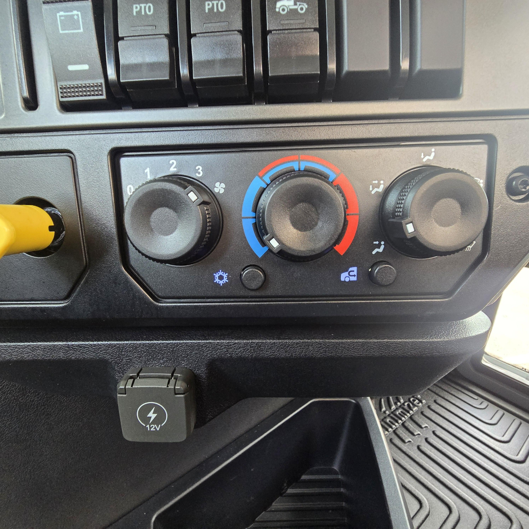 Truck interior showing climate control panel with three dials and a 12V plug in a Mack PI64T cab.