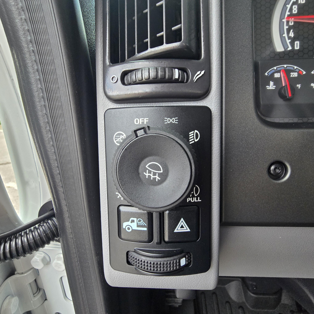 Dashboard controls panel in a Mack PI64T truck showing ignition/lighting switch and surrounding buttons with a graphic icon and traction control toggle.