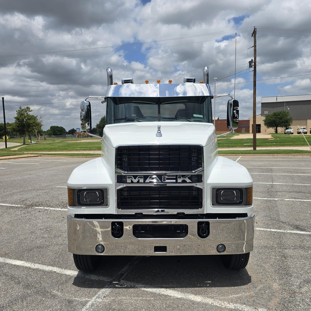 Truck front view showing Mack grille, large bumper with chrome finish, two rectangular headlights, and elevated cab.