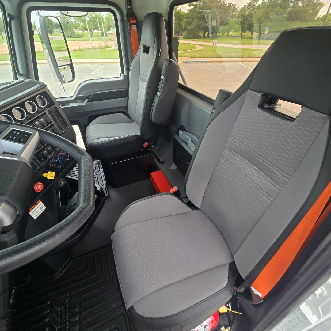 Cab interior of a 2027 Mack PI64T truck showing front seats and dashboard with steering wheel and gauges.