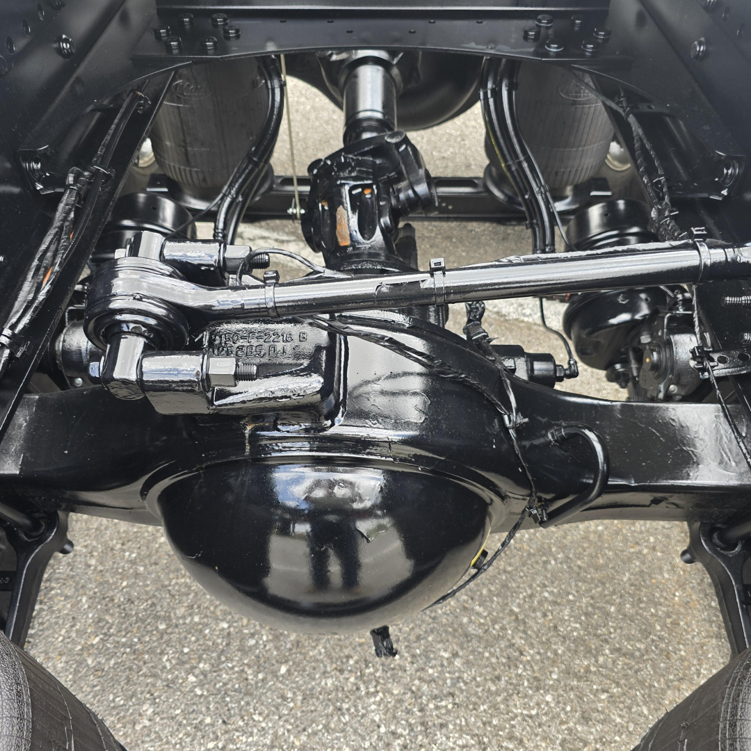 Rear underside of a new Mack PI64T showing solid axles, drive shaft, steering linkage, and differential housing.