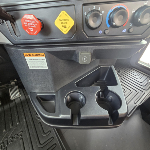 Dash area of a 2027 Mack PI64T cab showing parking brake yellow label, red trailer air supply knob, climate controls, and cup holders.