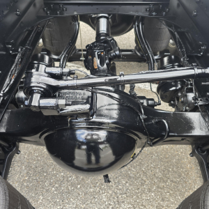 Rear underside of a new Mack PI64T showing solid axles, drive shaft, steering linkage, and differential housing.