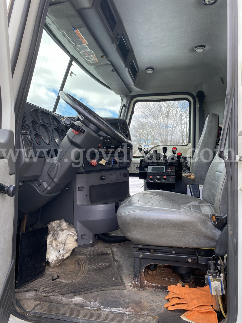 Cab interior of a Mack GU713 dump truck showing steering wheel, gauges, and driver seat with controls and floor mat.