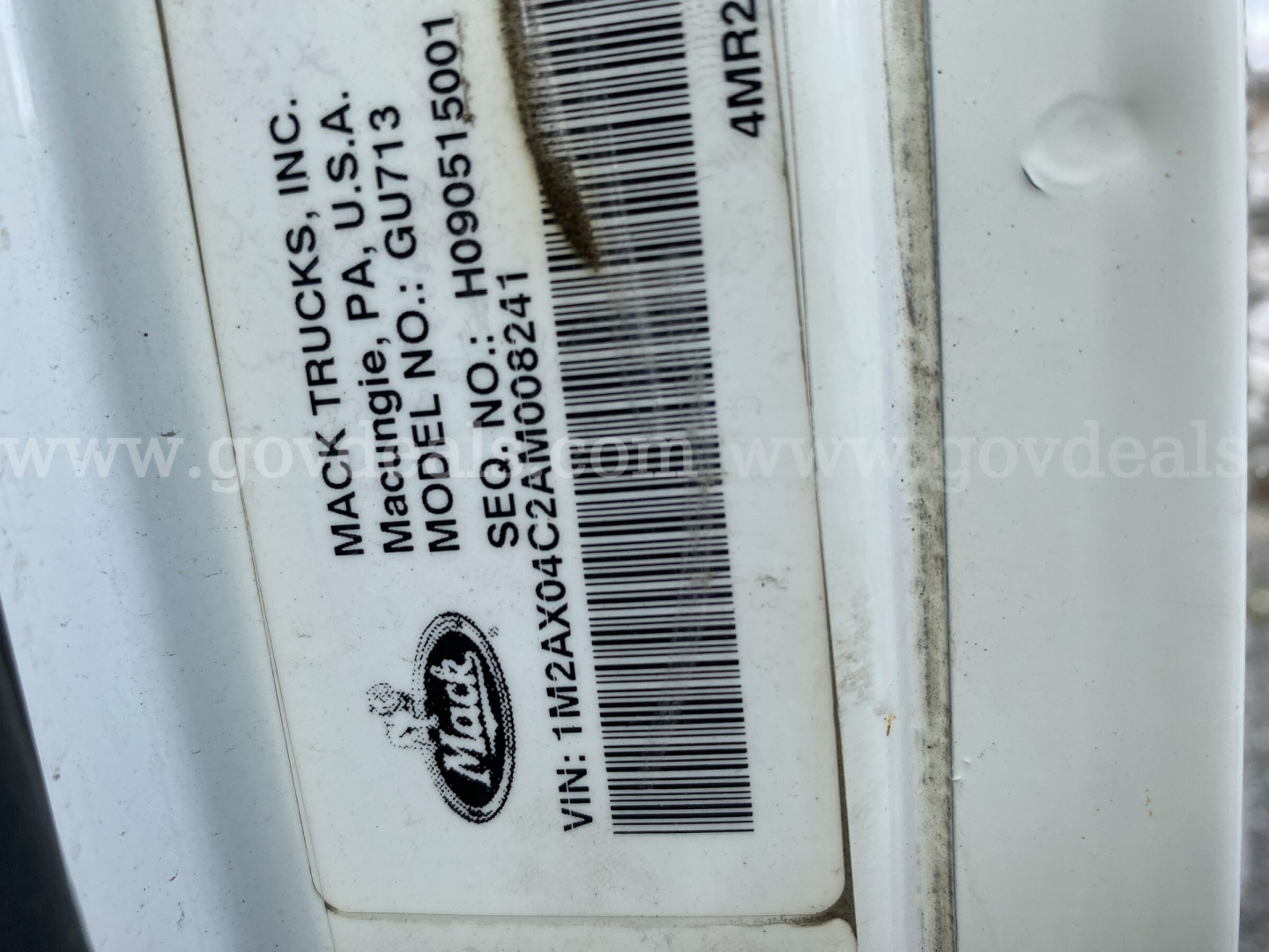 Mack Trucks VIN label on door showing Mack Trucks, Inc., model GU713, VIN 1M2AX04C2AM008241, serial/barcode, stock 11984-1880, dump truck category, used vehicle.
