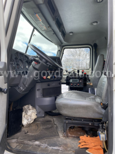 Cab interior of a Mack GU713 dump truck showing steering wheel, gauges, and driver seat with controls and floor mat.