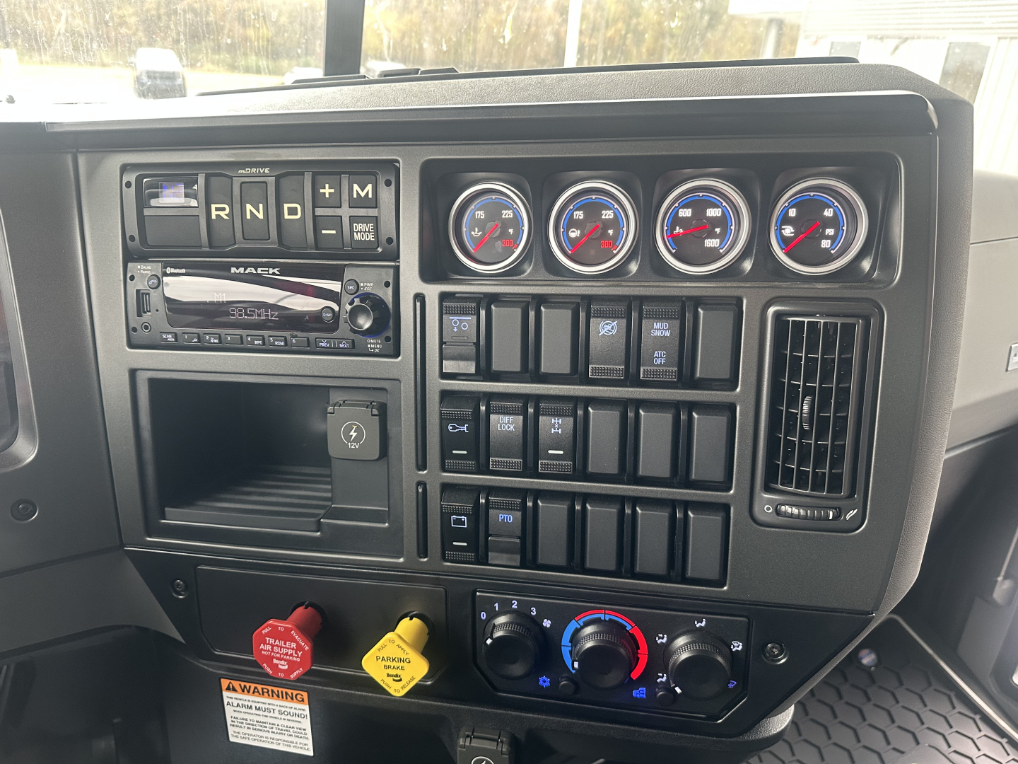 Dashboard panel of a 2026 Mack GR84F dump truck showing gauges, switches, and controls with an empty lower storage area and red/blue climate knobs.