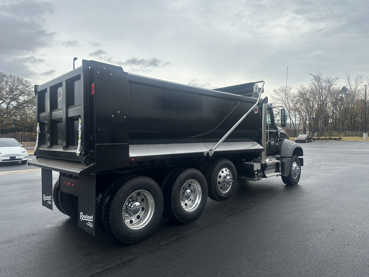 Dump truck with black Mack GR84F dump body showing side rails, wheels, and rear tailgate in a parking lot.