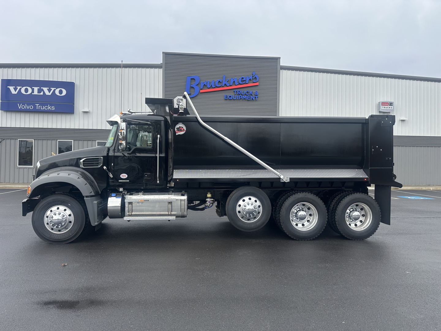 Dump truck side view showing 6x4 axle configuration and black dump body with chrome exhaust and logo on cab.