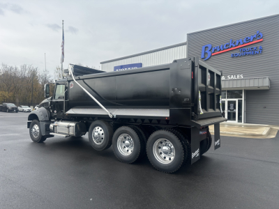 Dump truck in dealership lot showing Mack GR84F dump body with three axles and dual rear wheels; cab side mirrors; Brunkers sign in background.