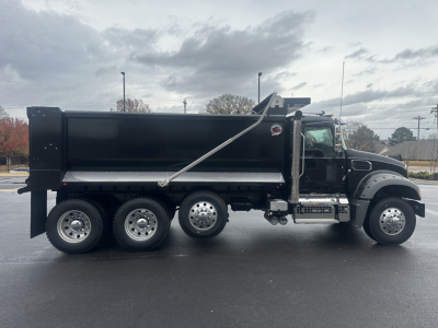 Side view of a black Mack GR84F dump truck showing the Dump body, rear hydraulic mechanisms, and six-wheeled axle configuration.