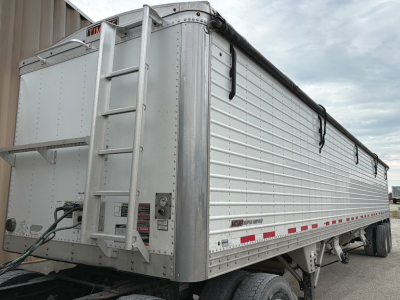 Trailer side and rear view of a 2018 Timpte Super Hopper in silver with ladder at rear, reflective striping along lower side, and spare components visible.