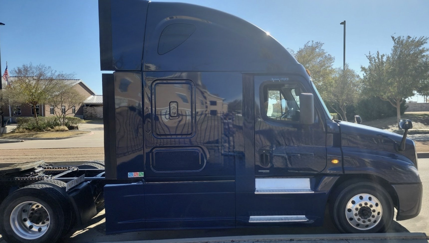Side view of a blue 2015 Freightliner Cascadia conventional sleeper truck showing the cab and wheel area with chrome accents.