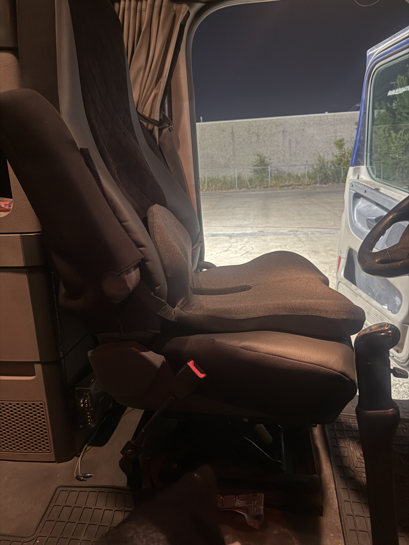 Cab interior of a freightliner truck showing a driver's seat in view, with steering wheel and open door; no additional text visible.
