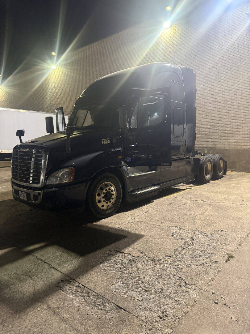 Truck tractor silhouette at night showing long hood, cab, and dual rear axles. Freightliner Cascadia cab with sleeper, black paint, headlight detail, and chrome wheel hubs.