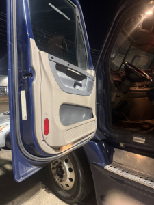 Truck cab interior and open door of a 2015 Freightliner Cascadia conventional sleeper. Visible text includes no explicit model text, just truck interior features.