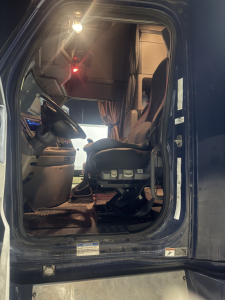 Cab interior of a Freightliner Cascadia truck showing driver seat and dashboard from open door.