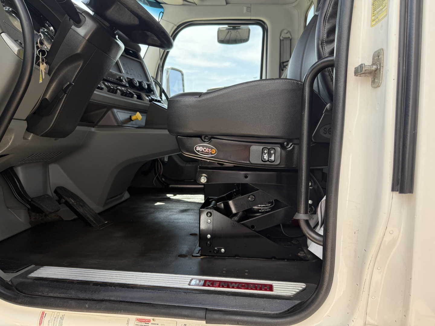 Kenworth T880 cab interior showing driver's seat with Kenworth base, floor mat, dash controls, and entry step.