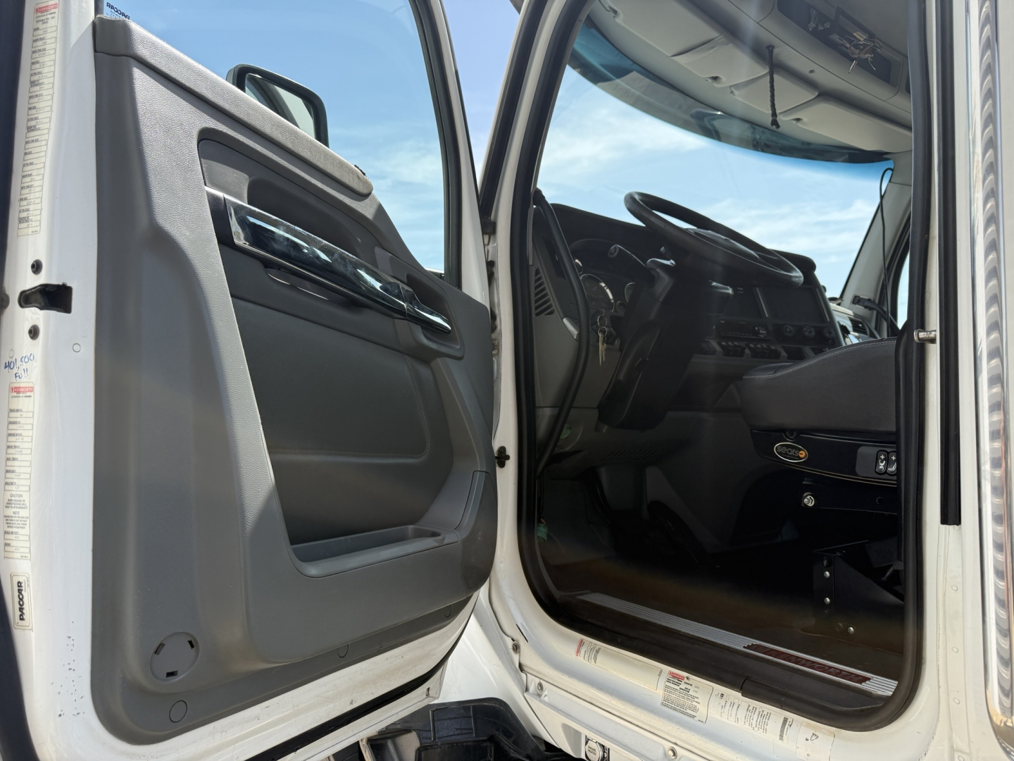 Kenworth T880 cab interior view with open driver door showing dashboard and steering wheel.
