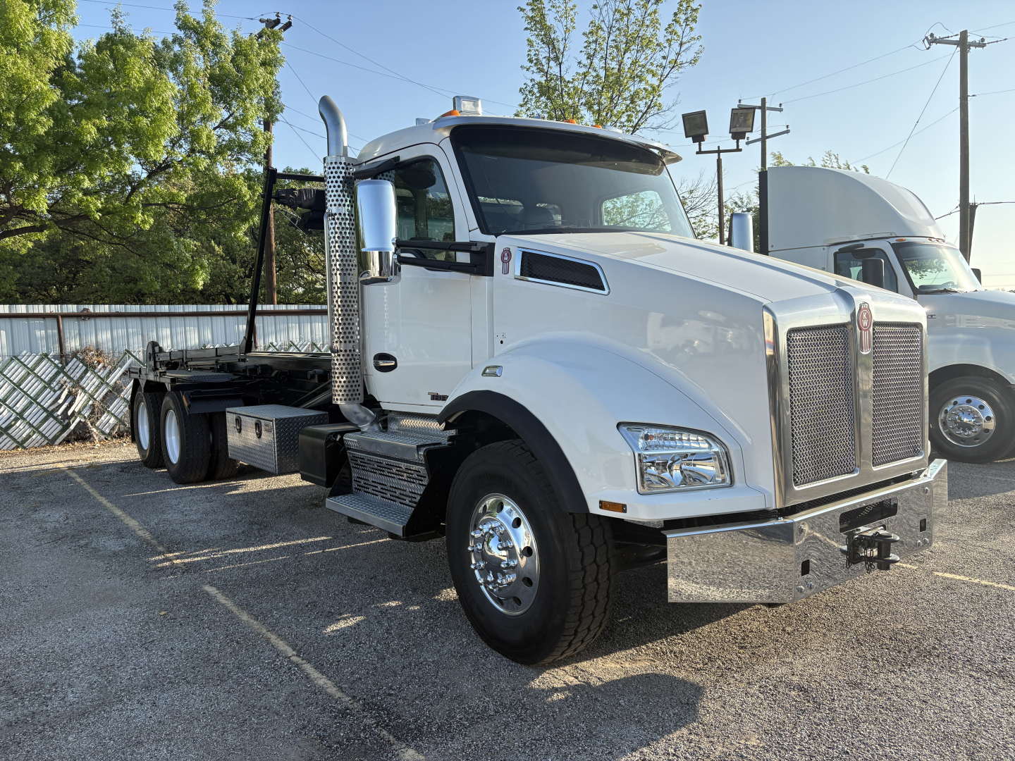 Kenworth T880 roll-off truck in white, front-right view showing chrome grille, chrome exhaust stack, front bumper, and dual rear axles.