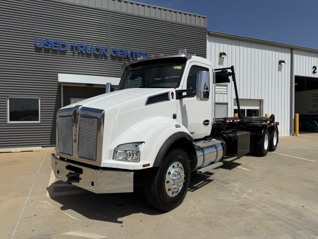 Kenworth T880 medium-duty truck in white, straight-on side view at a dealership, with roll-off configuration and chrome grille.