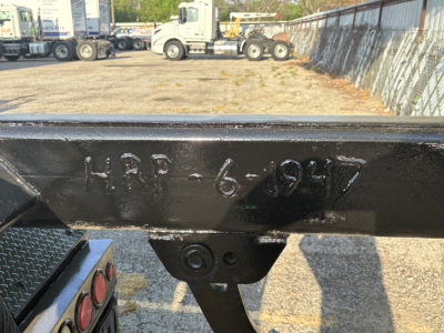 Metal frame of a roll-off truck showing stamped embossing 'HRP-6-9-17' on a black steel beam near a parking lot with other trucks in background.