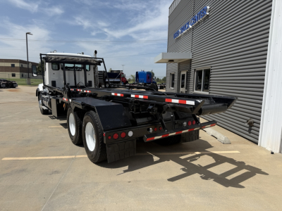 Kenworth T880 flatbed roll-off truck viewed from rear-left side showing dual rear axles and loading ramp in driveway.