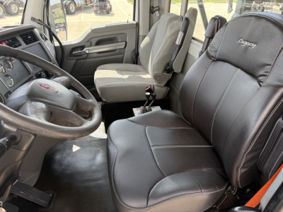 Truck cab interior of a 2018 Kenworth T880 showing steering wheel, driver and passenger seats, and dashboard with gear shifter; Legacy seat cover on passenger seat.