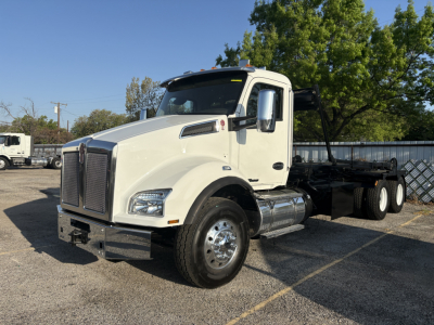 Kenworth T880 rolloff truck in a parking lot showing white cab and chassis with dual rear axles, front grille, and side mirrors.
