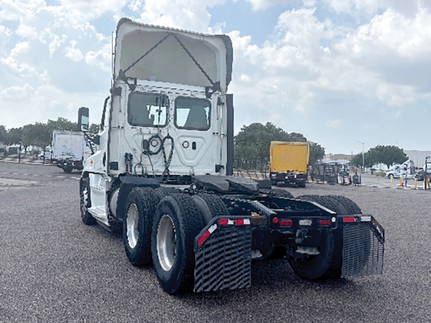 Truck tractor rear view showing Freightliner Cascadia 125 Evolution chassis with 4x4 rear axles and fifth wheel, no trailer attached, white cab with open sleeper compartment.