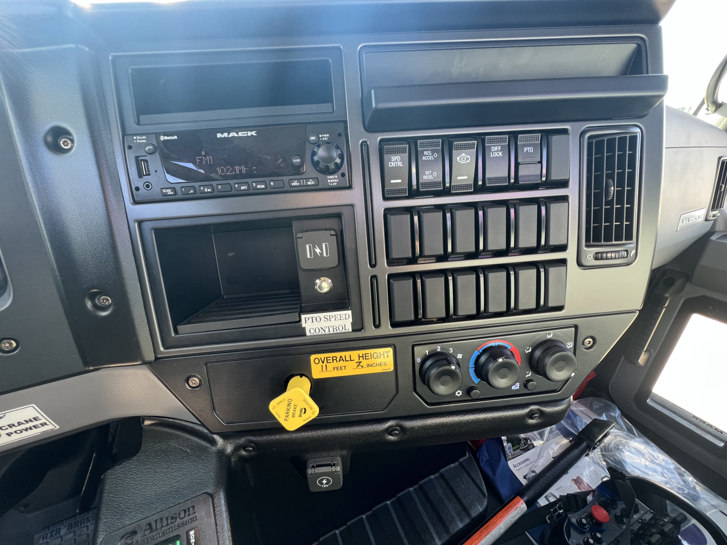 Mack MD7 cab interior showing dash with radio, multiple switches, and control knobs; labeled yellow tag near lower center.