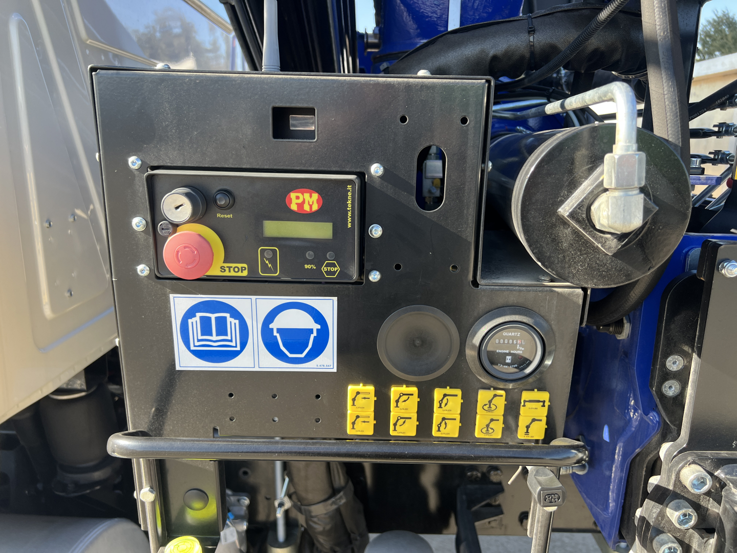 Operator control panel of a 2025 Mack MD7 boom truck showing a PM panel, STOP button, blue safety icons, and multiple yellow toggle switches.