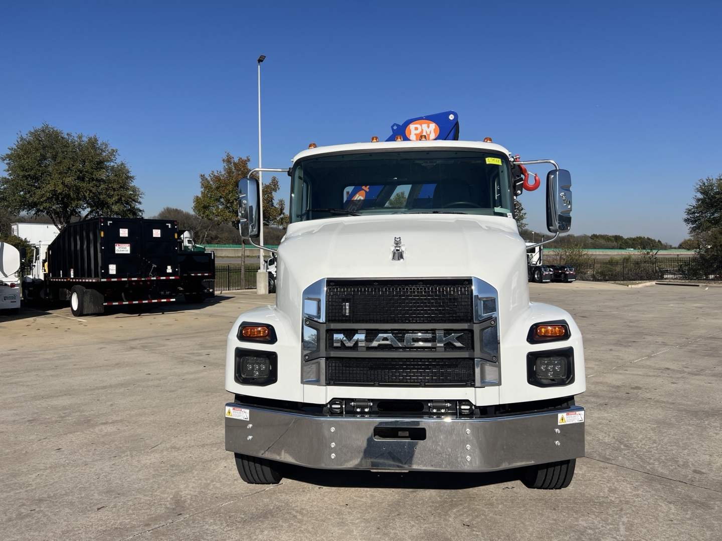 Mack MD7 front view showing bold grille with MAC K emblem, white cab, chrome bumper, dual rectangular headlights, and side mirrors in a parking lot.